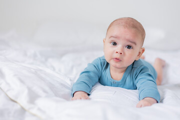 portrait of a cute baby in a blue bodysuit lying on his stomach to the bed. The child is 4 months old. Space for text
