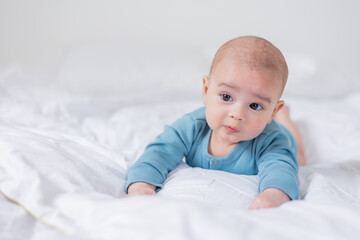 portrait of a cute baby in a blue bodysuit lying on his stomach to the bed. The child is 4 months old. Space for text