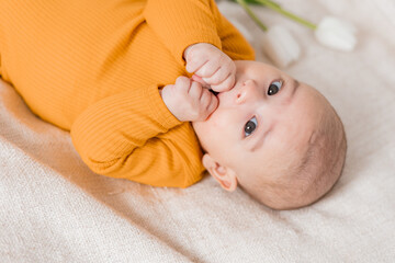 portrait of a cute baby in a yellow bodysuit lying on his back in a white bed. View from above. The child is 4 months old. Space for text