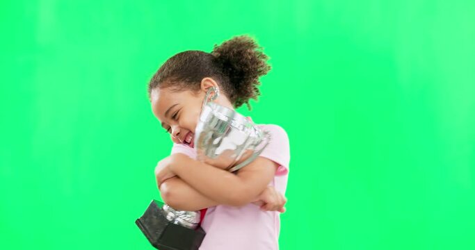 Happy, winning and face of child with a trophy isolated on a green screen studio background. Excited, success and portrait of a girl kissing an award for sports, achievement and champion with mockup