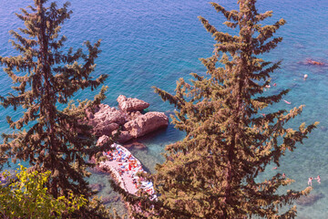 view through the pine trees on tourists from different countries relax on a narrow stone beach  among the warm clear waters of the Mediterranean Sea. Antalya. Turkey - 581901230
