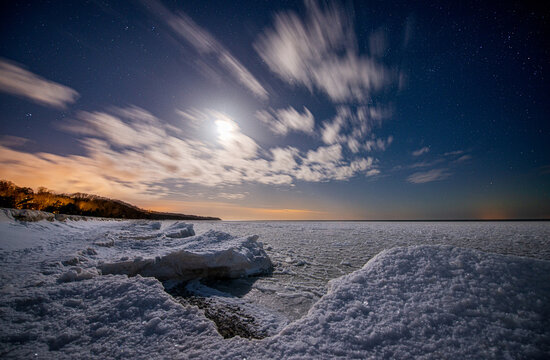 Seashore covered with ice under a starry sky with moon.