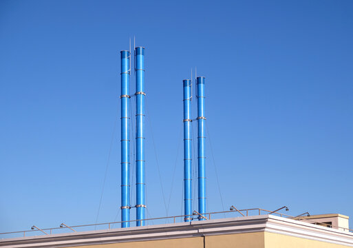 Four painted blue smoke stacks after roof of building on clear blue sky without clouds