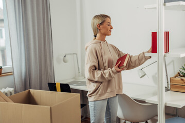 A young blond woman is placing books on a bookshelf