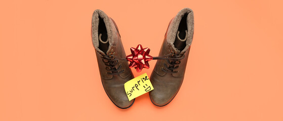 Paper with word SURPRISE, boots and ribbon bow on orange background. April Fools' Day celebration