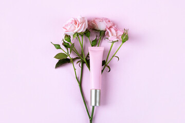 Cosmetic bottle container on a pink background with a roses. Top view of mockup of pink bottle plastic tube for branding of cosmetics gel, cream, skin care.