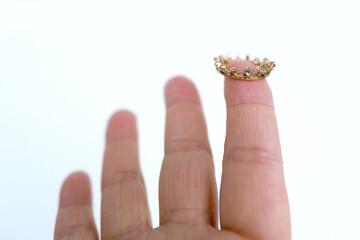 close up miniature metal silver crown, diadem on finger female hand, concept supreme power,...