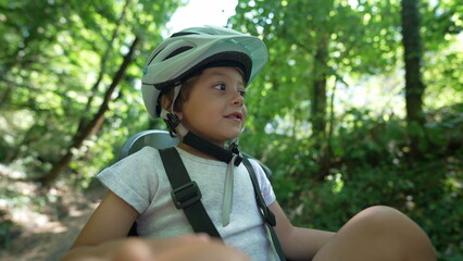 One adorable little boy wearing helmet seated in bicycle chair at nature park. Happy child enjoying weekend activity