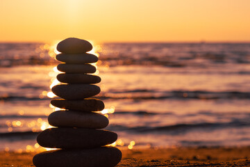 Balanced pebble pyramid silhouette on the beach on sunset with Sea on the background. Zen stones on the sea beach, meditation, spa, harmony, calmness, balance concept.