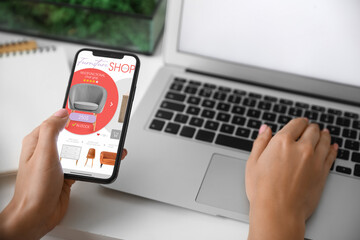 Woman with mobile phone and laptop buying online new furniture