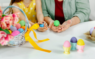 the hands of an elderly woman and a child hold a colored Easter egg