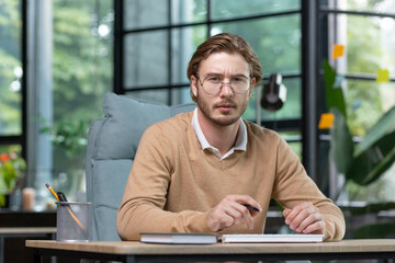 Portrait of a creative office worker sitting at a table with a computer, looking seriously at the...
