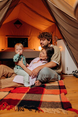 Obraz na płótnie Canvas Happy family with lovely baby playing and spend time together in glamping on summer evening. Luxury camping tent for outdoor recreation and recreation. Lifestyle concept