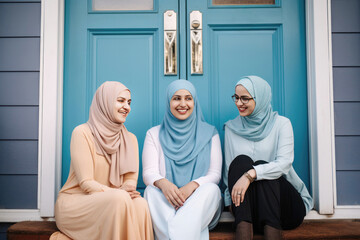 Obraz premium Three happy teenage women wearing hijabs sitting outside and talking (Generative AI)
