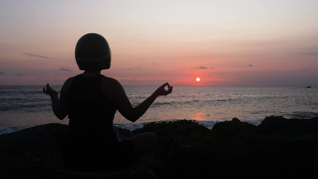 Silhouette of a biker girl meditating by ocean at sunset. Medium close up.