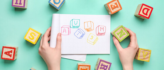 Female hands, notebook with word AUTISM and cubes on color background