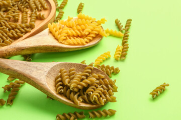 Wooden spoons with raw fusilli pasta on green background, closeup