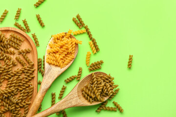 Wooden board and spoons with raw fusilli pasta on green background