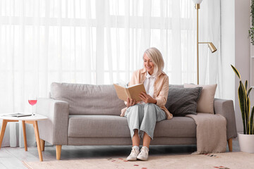 Mature woman reading book on grey sofa at home