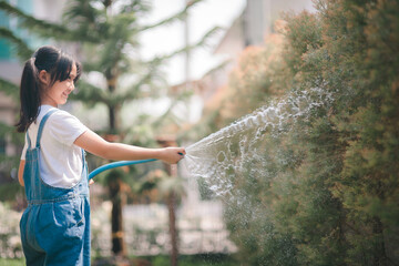 Asian little child girl water the plants. kid helps to care for the plants in the garden.