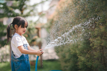 Asian little child girl water the plants. kid helps to care for the plants in the garden.