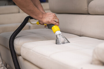 Cleaning a dirty sofa with a sofa washer. Close up of hands holding sofa cleaner. Professional sofa...
