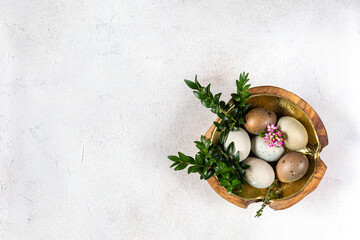 Six Easter eggs decorated with boxwood and small pink flowers lie in a wooden bowl with a gold...