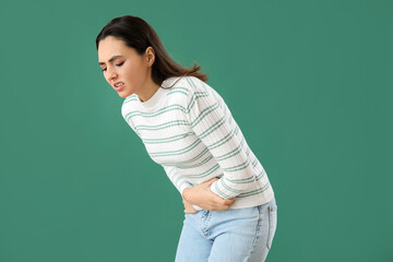 Young woman with abdominal pain on green background