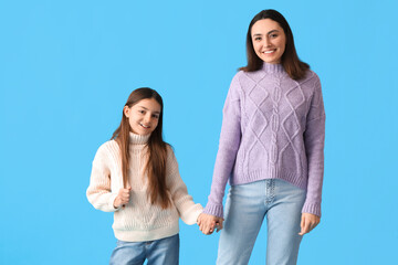 Little girl and her mother in knitted sweaters holding hands on blue background