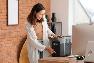 Young woman with portable power station at table in office