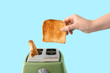 Woman taking crispy bread slice from modern toaster on blue background
