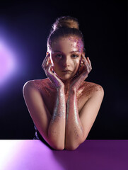 Beautiful young woman with glitter makeup at purple table on dark background