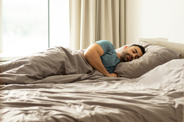 Caucasian man sleeping in bed on side, lying under blanket, napping at home, resting peacefully in...