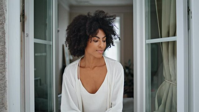 African woman peeping window at home closeup. Curly girl looking camera portrait