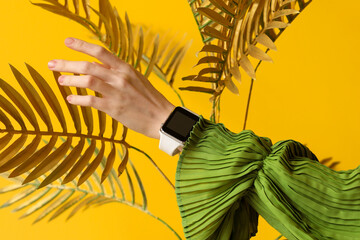 Woman with smartwatch and golden palm leaves on yellow background