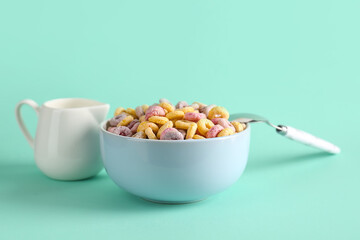 Bowl of colorful cereal rings and pitcher with milk on turquoise background