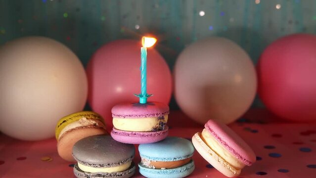 Colorful macarons and one candle on blue and pink background with decorations, happy birthday concept 