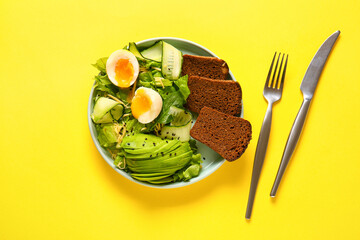 Plate of delicious salad with boiled eggs and avocado on yellow background