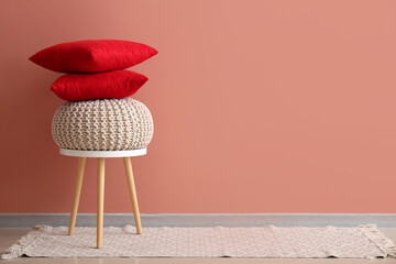 Stack of stylish decorative pillows and pouf on stool near pink wall