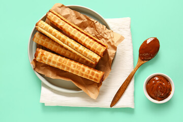 Plate of delicious wafer rolls with boiled condensed milk on turquoise background