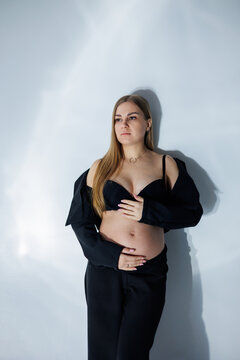 Cute pregnant woman in studio. Pregnant woman in a black suit. Happy pregnant woman - pregnant photo of beautiful young expectant mother on gray background, studio photo