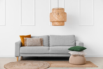 Interior of light living room with grey couch, pouf and pillows