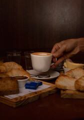 typical Argentinian snack with coffee, croissants, orange juice, cheese and ham on a wooden tray and a wooden table and someone holding a cup of coffee: horizontal image