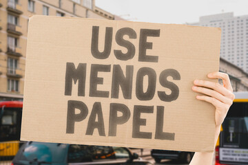 The phrase " Use less paper! " on a banner in men's hands with blurred background. Human impact on the environment. Environmental degradation. Nature. Forest. Trees. Modern technology