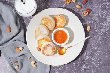 Plate with tasty cottage cheese pancakes, jam, milk and nuts on grunge background