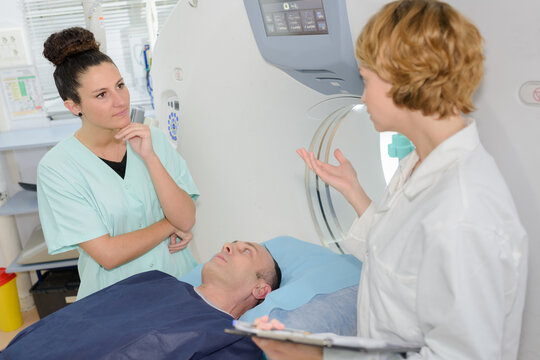 female medics in discussion across male patient layed on scanner
