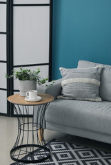 Grey sofa with cushion and houseplant on table near blue wall