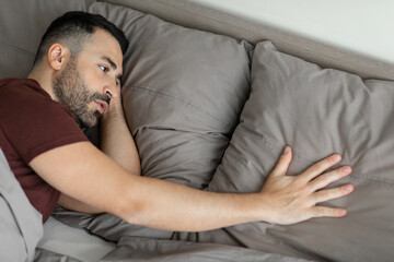 Sad middle aged man touching pillow, suffering from loneliness after breakup, lying in bed at home, above view, free space. Lonely male having depression