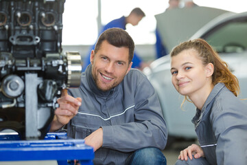 smiling young woman mechanic in overalls next to teacher