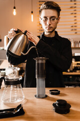 Barista is pouring hot water from drip kettle to aeropress. Process of brewing aeropress. Pouring hot water over roasted and ground coffee beans in aeropress.
